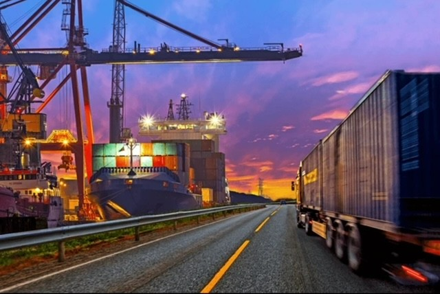 A truck driving down the road near a large ship.